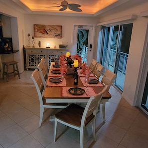 A dining area with a table set for four, chairs, a ceiling fan, a kitchen area with a cabinet, and a painting on the wall.