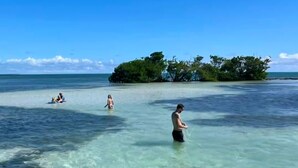 A beach scene with clear shallow water, a small island with trees, and people swimming. - Sunchasers Paradise - lux home, private pool/spa, 80' dock (Marathon)