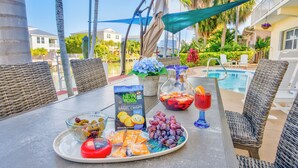 A table set with snacks, a drink, and a bagel box at a poolside area with wicker chairs and a view of the pool and greenery. - Sunchasers Paradise - lux home, private pool/spa, 80' dock (Marathon)