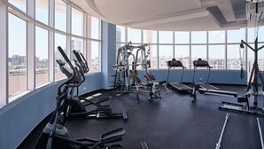Un gimnasio con diverso equipo de ejercicio, amplias ventanas y vistas a la ciudad.