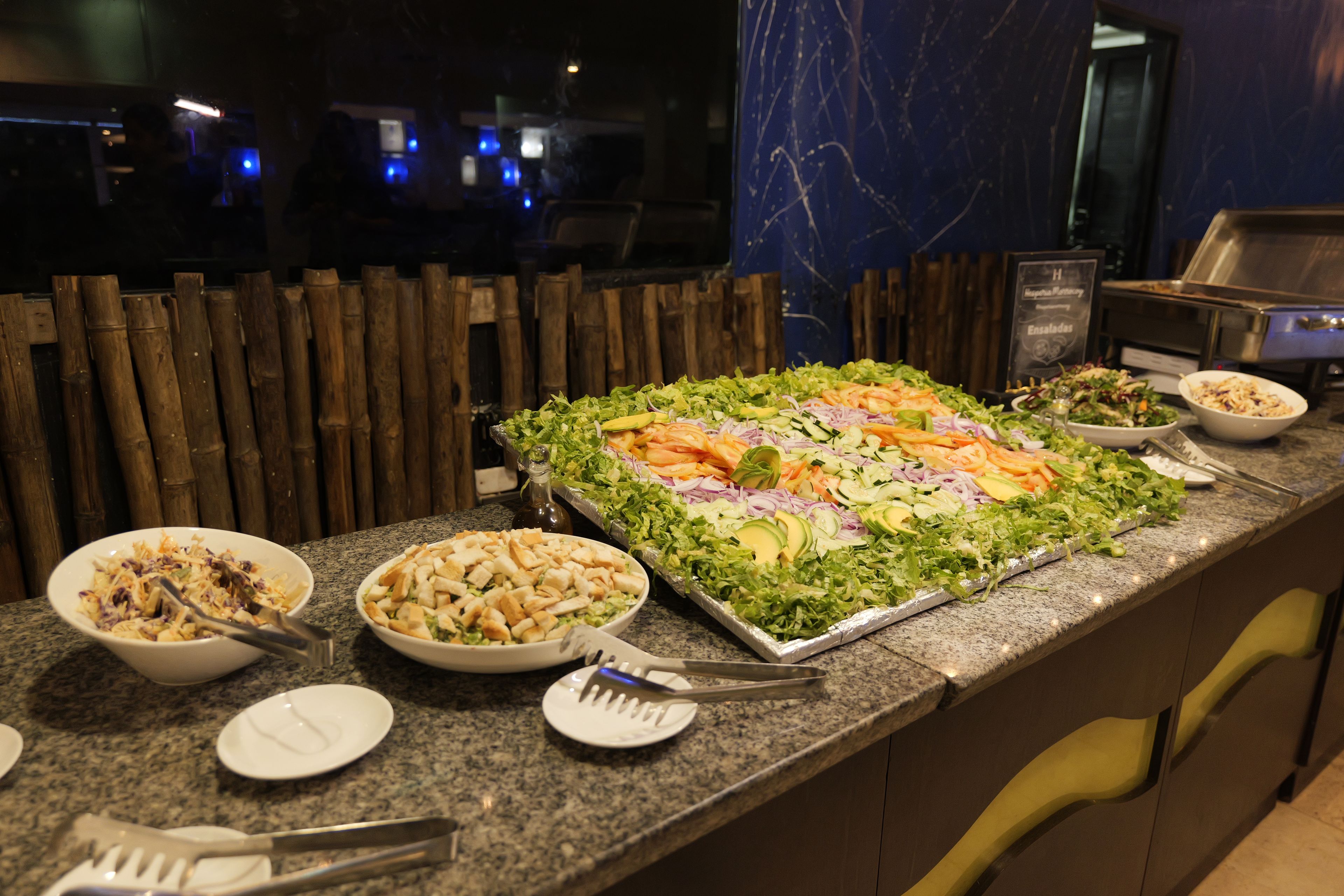 A buffet with various salads and dishes, a wooden fence in the background, and a marble countertop.