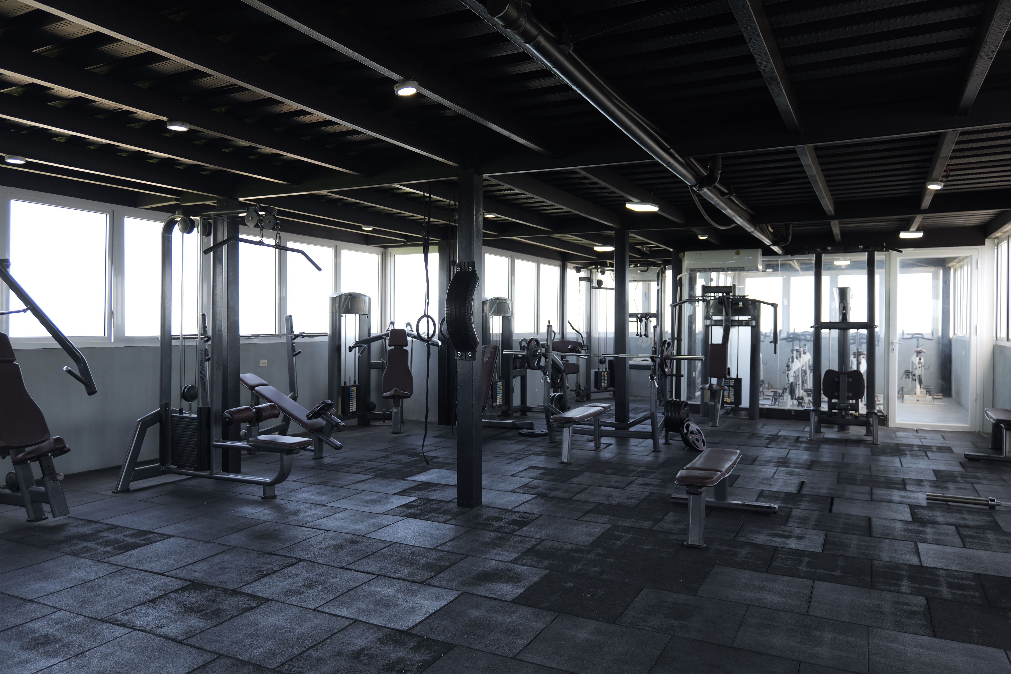 A gym with various exercise equipment, large windows, and a tiled floor.