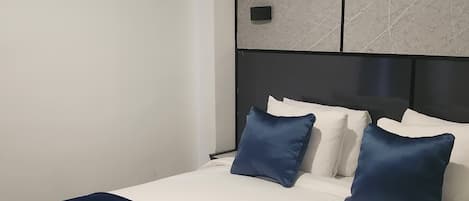 A hotel room with a large bed, white bedding, a dark blue throw blanket, and a modern air conditioning unit on the wall.