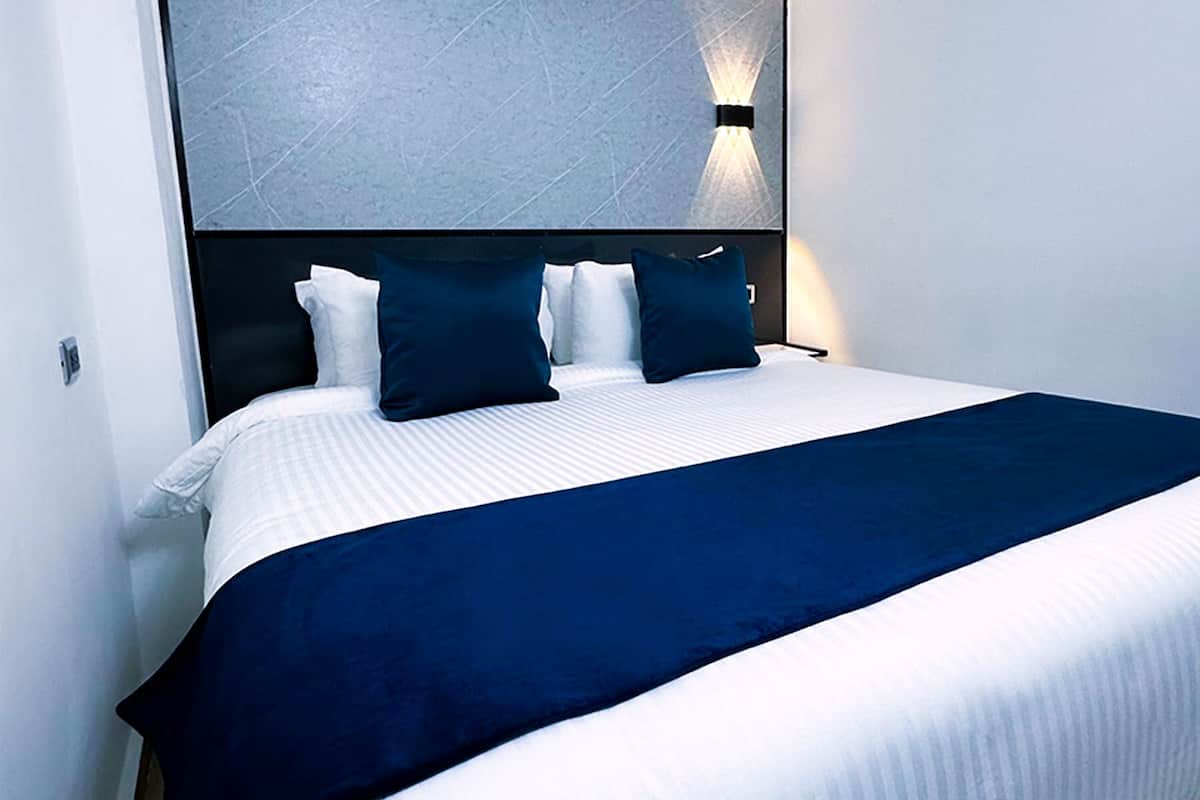 Een hotelkamer met een net opgemaakt bed, een grote spiegel boven het bed en een wandlamp.