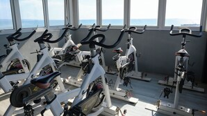 Varias bicicletas estáticas en un gimnasio con amplias ventanas que dan al mar.