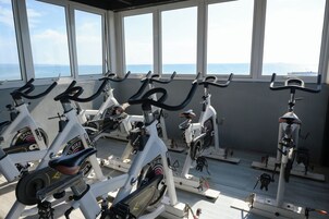 Varias bicicletas estáticas en un gimnasio con amplias ventanas que dan al mar.