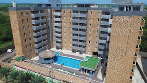 Un hotel de varios pisos con piscina central, mobiliario exterior y vistas del paisaje circundante.