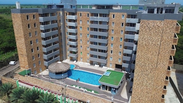Un hotel de varios pisos con piscina central, mobiliario exterior y vistas del paisaje circundante.
