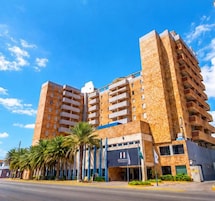 Un hotel de varios pisos con diseño moderno, que cuenta con balcones en cada planta y una entrada destacada con un letrero.