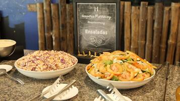Bancada de restaurante com duas saladas em tigelas, um menu em lousa e talheres.