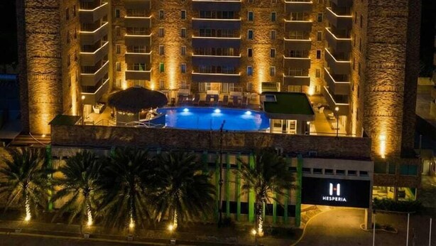 Un hotel de varios pisos con piscina al frente, fachada de piedra y balcones iluminados.