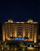 Un hotel de varios pisos con piscina al frente, fachada de piedra y balcones iluminados.