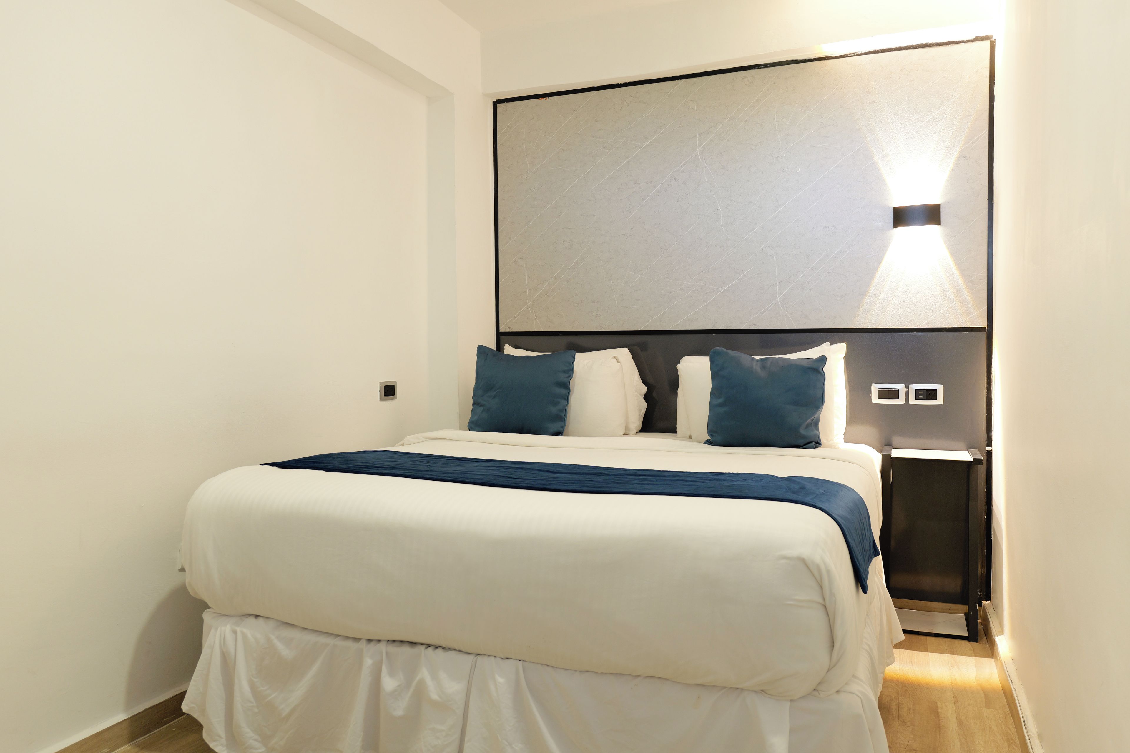 Una habitación de hotel con una cama grande, una mesita de noche, una lámpara de pared y un diseño moderno.