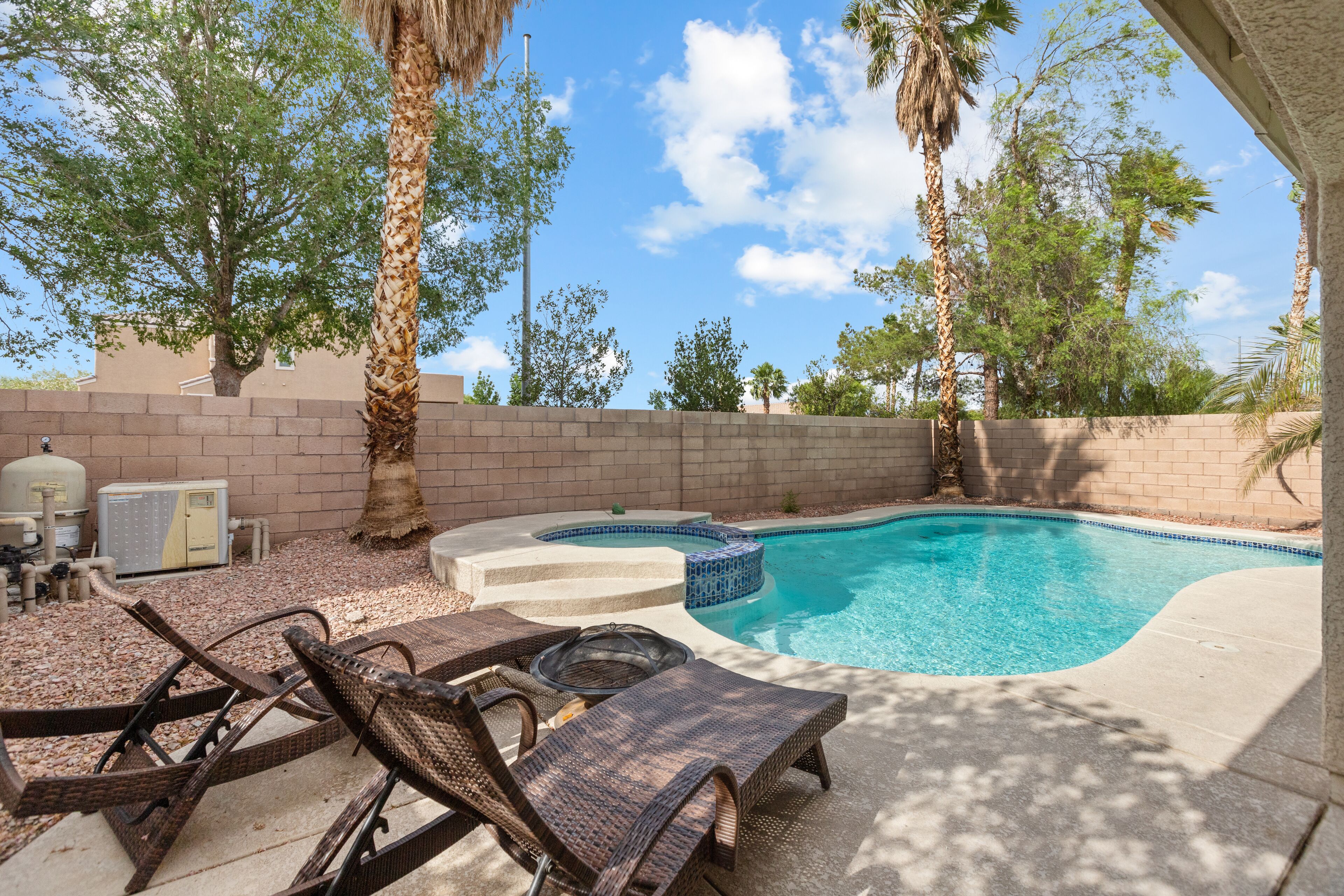 A backyard with a swimming pool, lounge chairs, and a hot tub.