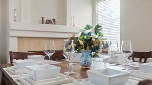 Et spisebord dækket med hvide, firkantede tallerkener, klare vinglas og en dekorativ vase med blomster.