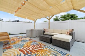 Une terrasse extérieure avec des meubles en osier, un tapis à motifs et un auvent.