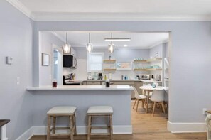 Une cuisine moderne dotée d’un îlot central, de tabourets de bar, de luminaires suspendus et d’un coin repas avec des chaises et une table.