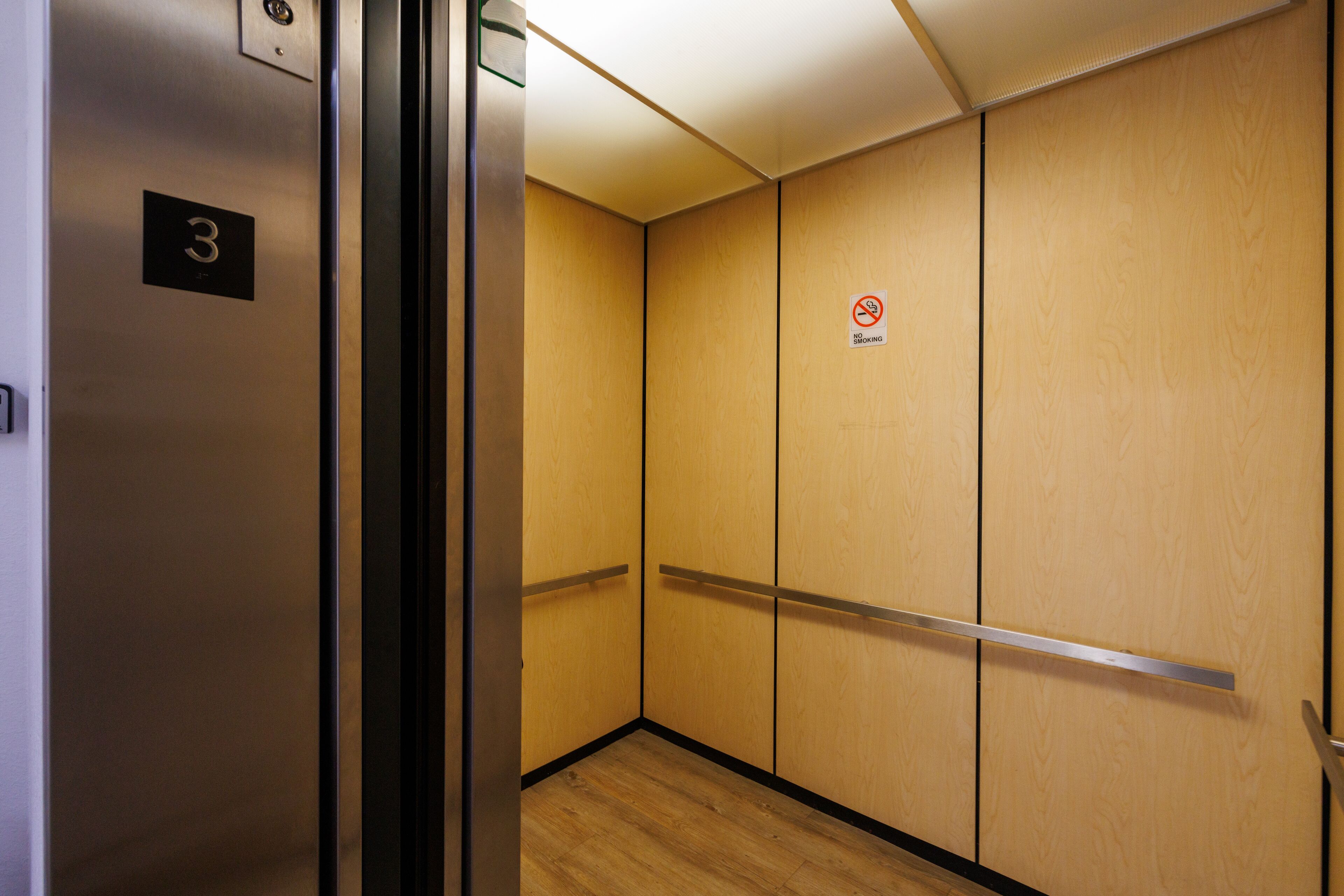 Un ascenseur avec un intérieur en bois, un panneau indiquant «Interdiction de fumer » et le chiffre «3» peint sur le mur.