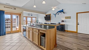 A spacious kitchen with a large island, wooden cabinets, and a ceiling fan. - OBX Top-Floor Condo- Marina & Sound Views, Quiet & Serene (Manteo)