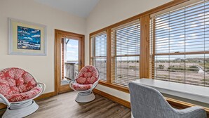 A room with two rocking chairs, a bench, and large windows with blinds. - OBX Top-Floor Condo- Marina & Sound Views, Quiet & Serene (Manteo)