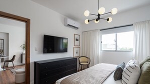 A modern bedroom with a bed, a dresser, a television, and a window with curtains.