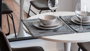 A dining area with a round table set for two, featuring white plates, bowls, and glasses.
