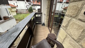 A balcony with a wooden railing, a single brown plastic chair, and a stone wall.