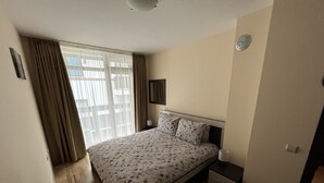A bedroom with a bed, a bedside table, a lamp, and a window with curtains.