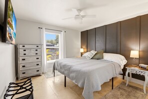 A bedroom with a bed, a dresser, a chair, a nightstand, a lamp, and a ceiling fan.
