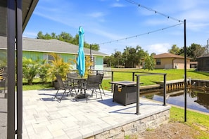 Eine Terrasse im Freien mit Tisch und Stühlen, einem blauen Sonnenschirm und einer kleinen Mülltonne.