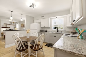 A modern kitchen with white cabinetry, a granite countertop, and a dining area with a wooden table and white chairs.