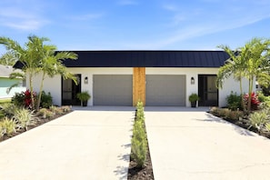Ein modernes, zweigeschossiges Haus mit Garage, Auffahrt und gepflegtem Garten mit Palmen und Sträuchern.