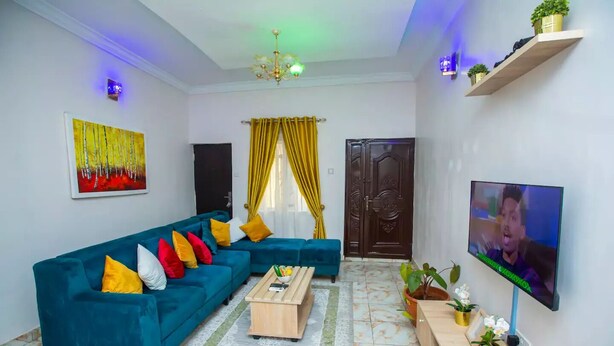 A living room with a blue sofa, a coffee table, a TV, and decorative plants. - AJI (1.0)| Luxury 3BED Apartment (Ijegun, Lagos) (Lagos)