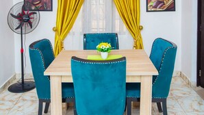A dining area with a wooden table and teal upholstered chairs, yellow curtains, and a ceiling fan. - AJI (1.0)| Luxury 3BED Apartment (Ijegun, Lagos) (Lagos)