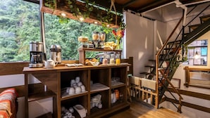 Quarto aconchegante com prateleira de madeira exibindo utensílios de cozinha, uma cafeteira e vista para um verde exuberante.