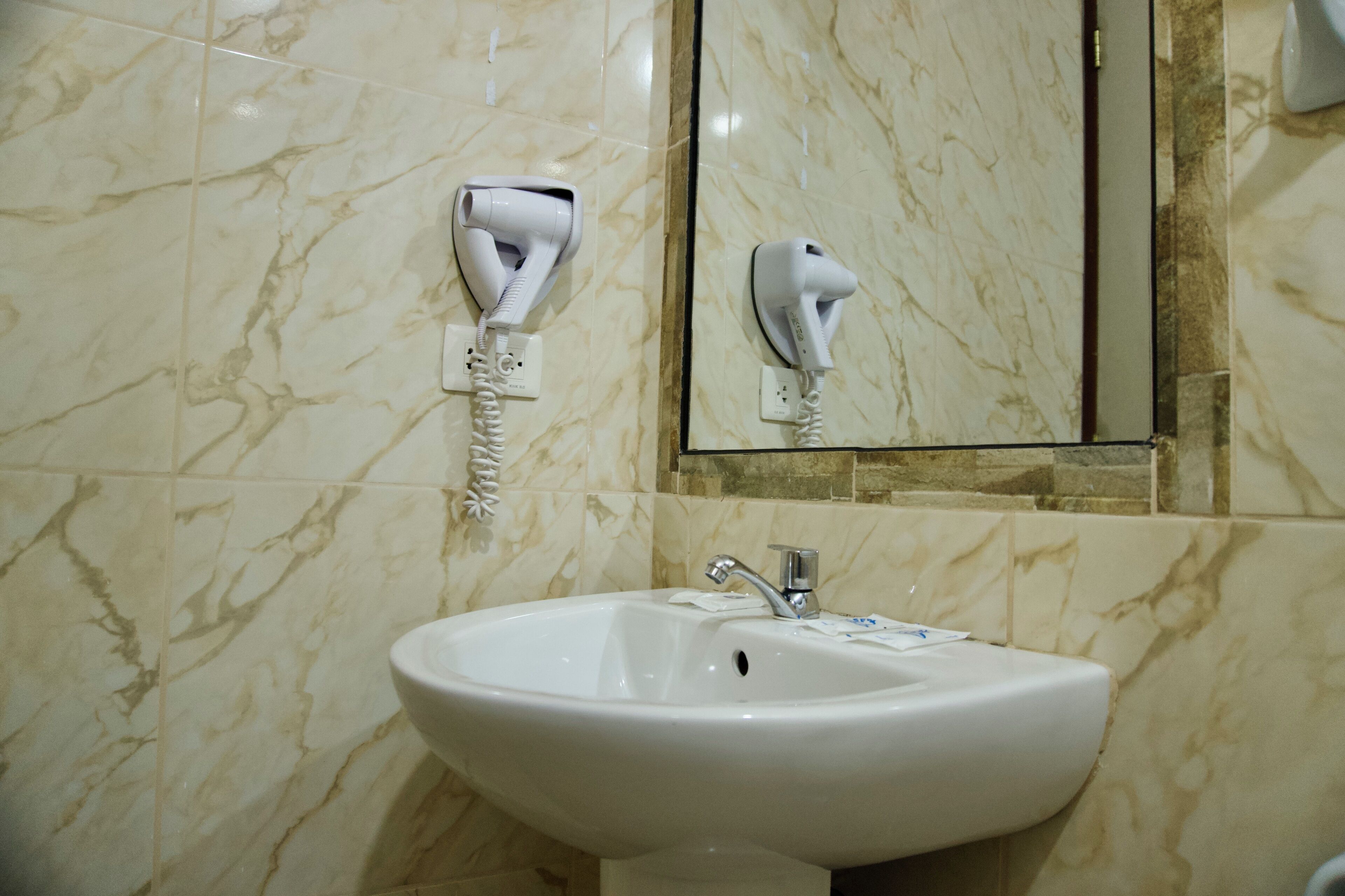Un bagno con parete in marmo, lavandino bianco e asciugacapelli montato a parete.