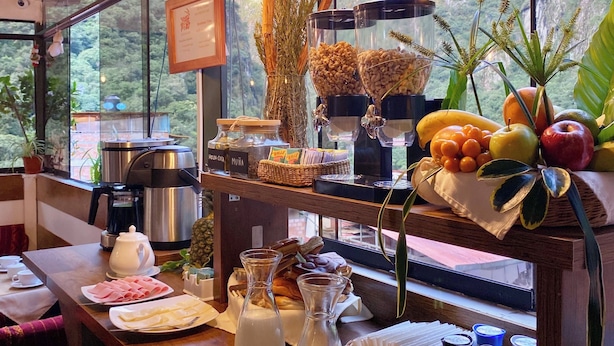 Um buffet de café da manhã com diversos alimentos, uma máquina de café e vista para montanhas através de amplas janelas.