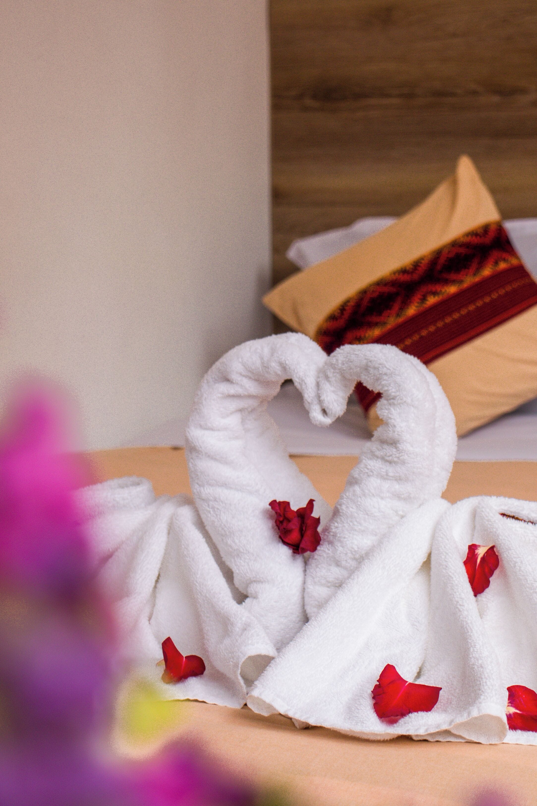A bed with a heart-shaped towel arrangement and a decorative pillow.