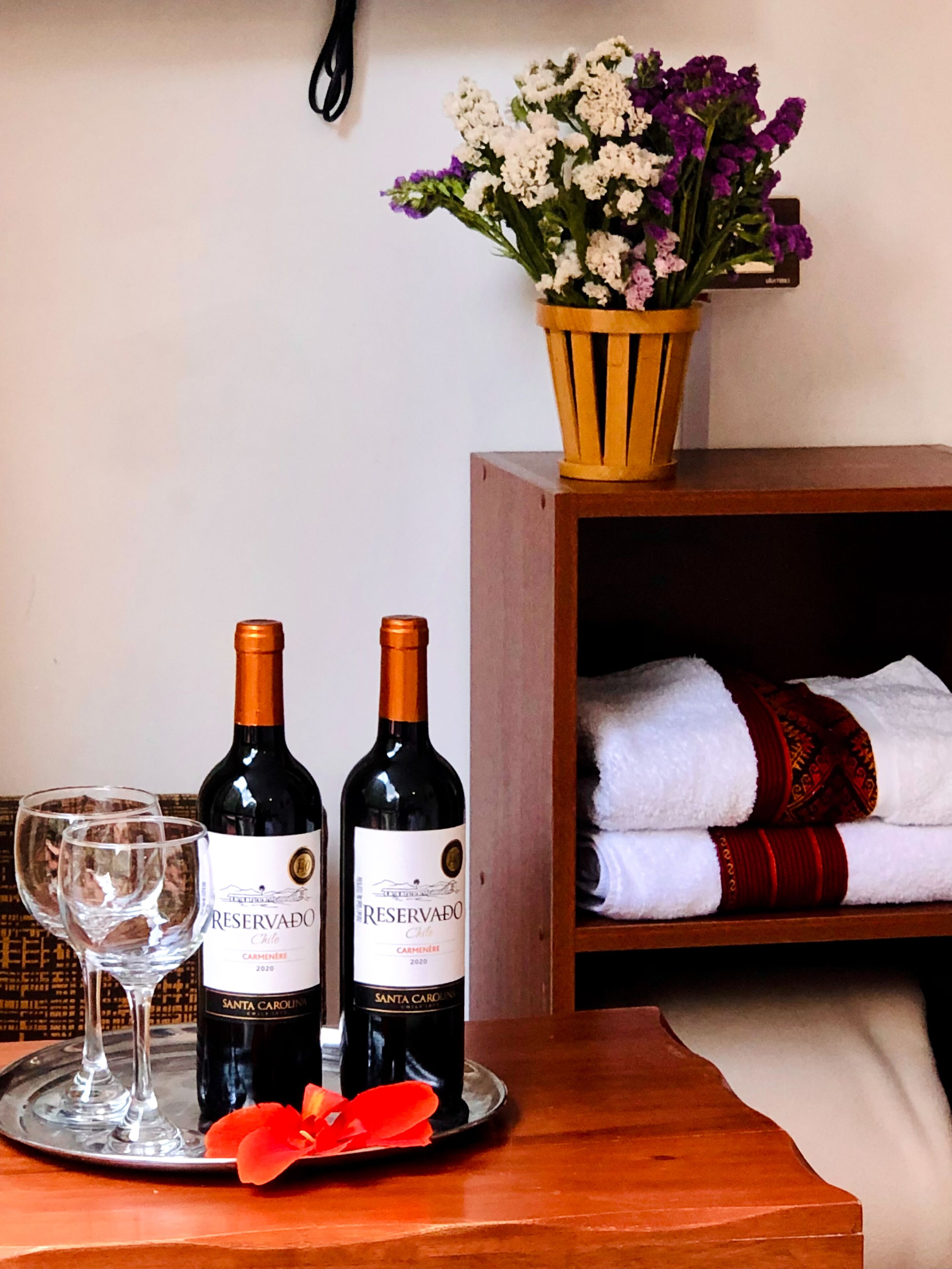 A table with two bottles of wine, a glass, and a flower on a tray.