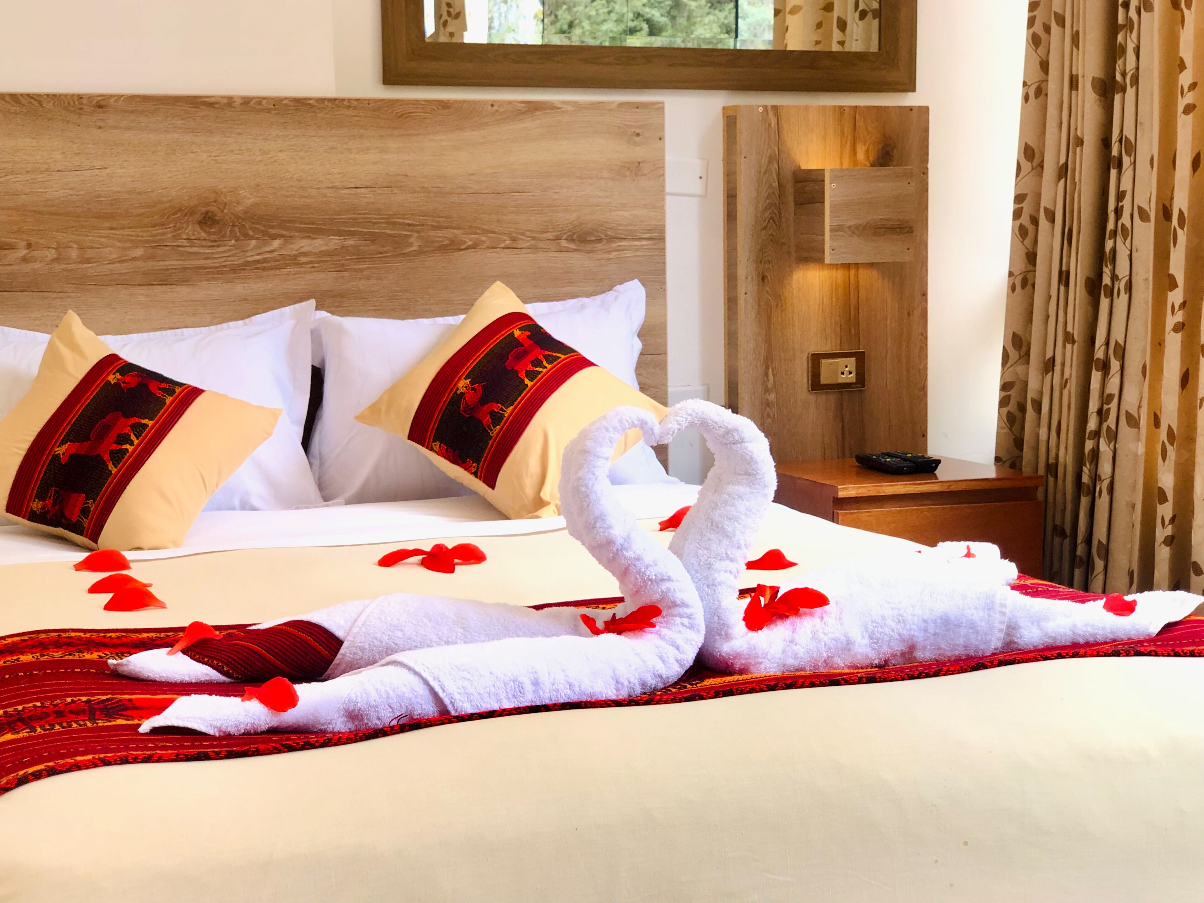 Cama bem arrumada com lençóis brancos e almofadas vermelhas, cabeceira de madeira e luminária fixada na parede.