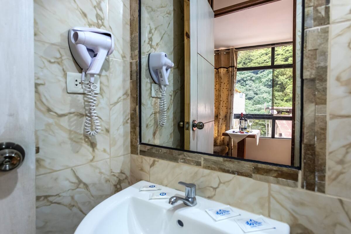 Un baño con pared de mármol, un lavamanos con espejo y un secador de pelo montado en la pared.