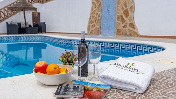 A poolside setting with a bowl of fruit, a bottle of wine, a glass, a towel, and a magazine. - Villa Mediluzma Almuñécar by Ruralidays (Granada)