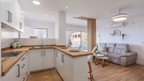A modern kitchen with white cabinets, a wooden countertop, and a built-in stove. There is a dining area with a table and chairs, and a sofa in the living room. - Villa Mediluzma Almuñécar by Ruralidays (Granada)