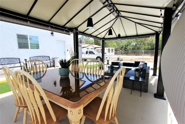 Eine überdachte Terrasse mit einem Holztisch und -stühlen, einem Blumentopf und einer Sitzecke mit Sofa und Sesseln.