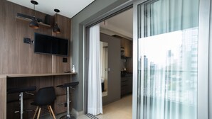 A modern kitchen with a flat-screen TV, wooden cabinets, and a sliding glass door leading to a balcony with a city view. - 360 VN Vergueiro (São Paulo)