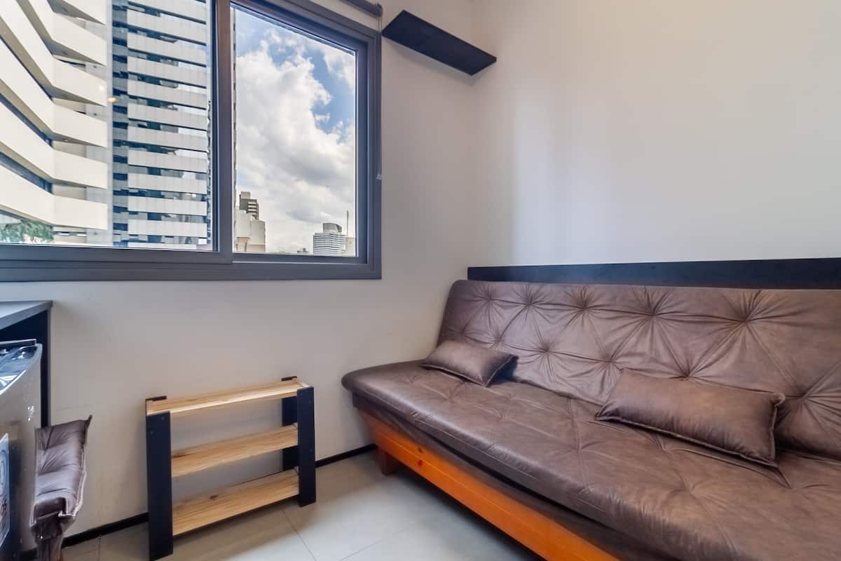 Uma sala de estar moderna com um sofá de couro marrom, um banco de madeira e uma grande janela com vista para o horizonte da cidade.