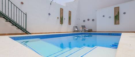 A swimming pool with a tiled edge, a staircase, and a chair by the pool.
