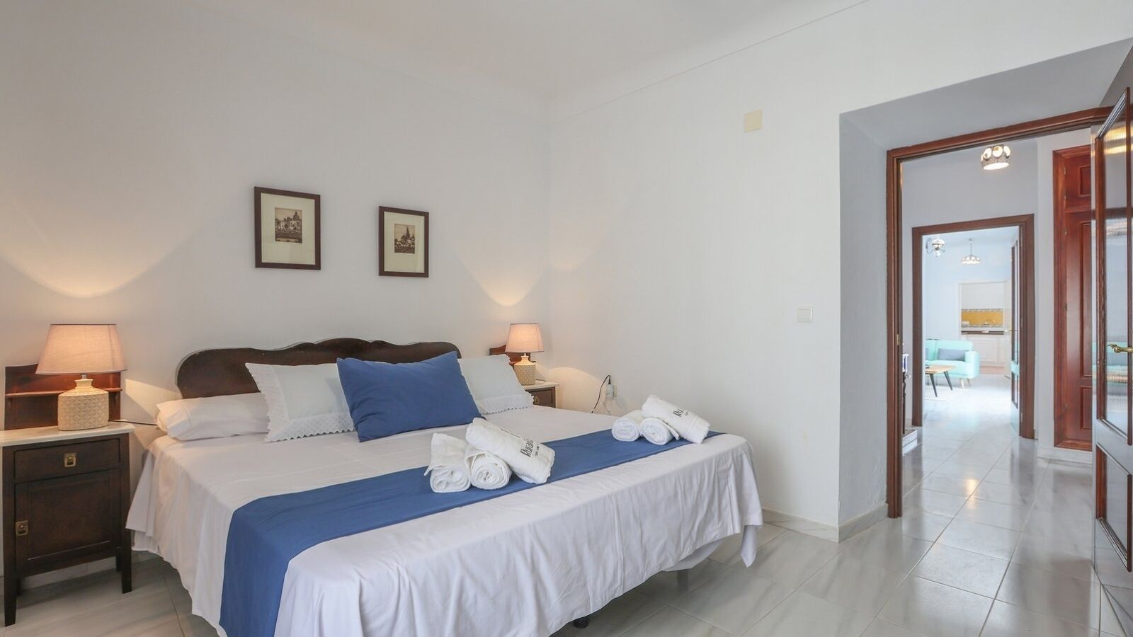 A hotel room with a bed, two bedside lamps, a nightstand, and a blue throw blanket.