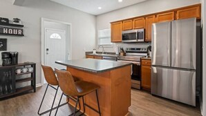 Una cocina moderna con armarios de madera, electrodomésticos de acero inoxidable y una zona de bar con taburetes.