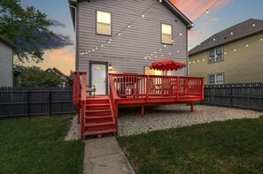 Une maison avec une terrasse rouge, un petit porche et une allée gravillonnée.